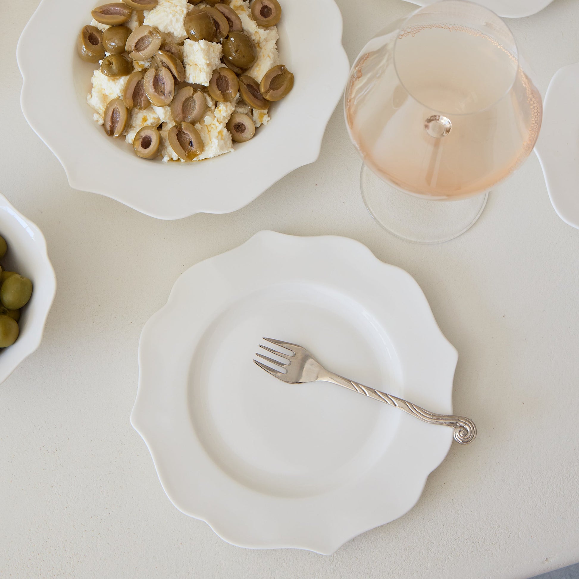 Dessert plates with various pastries and a glass of white wine on a light surface.