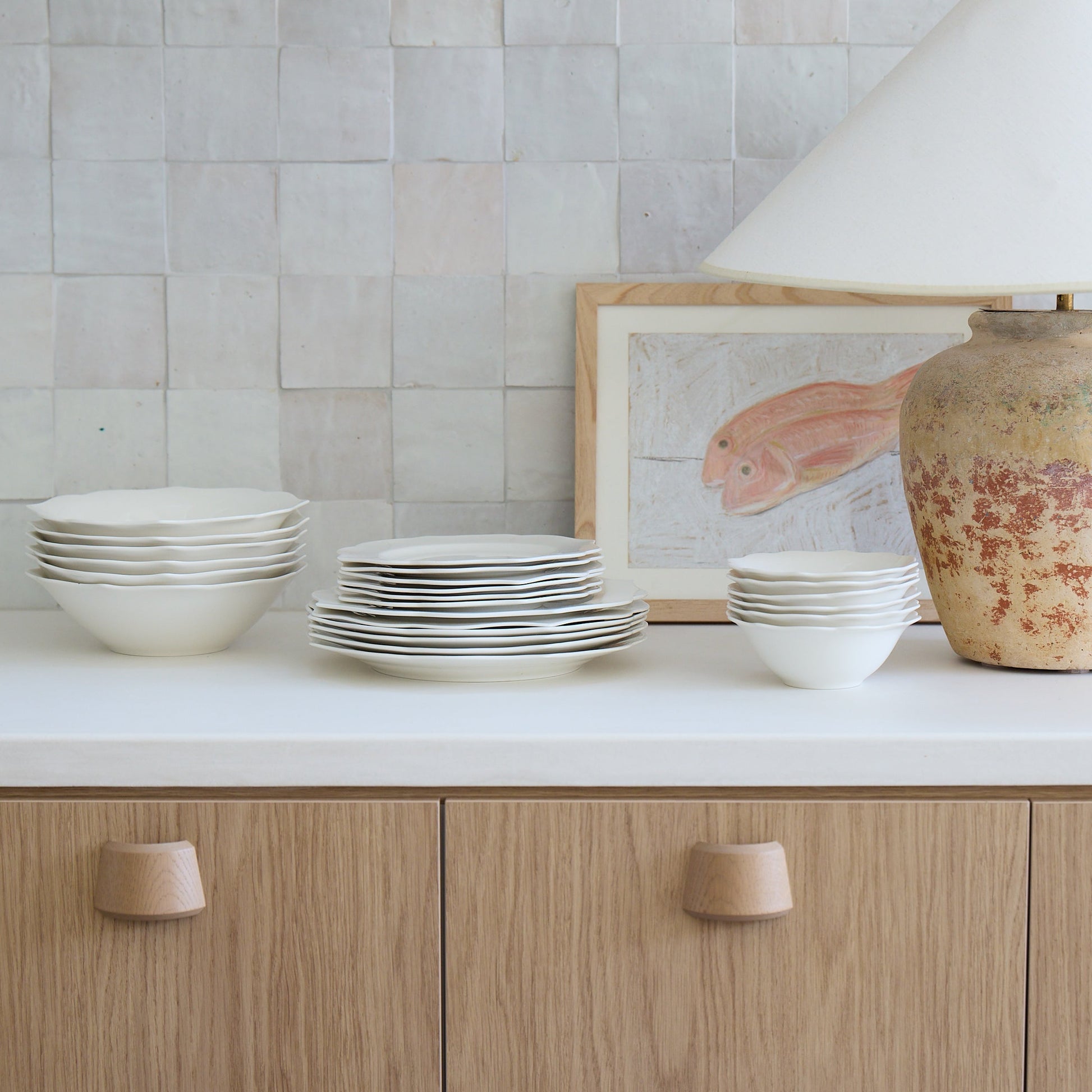 Ceramic tableware on a kitchen counter with a lamp and framed picture in the background.