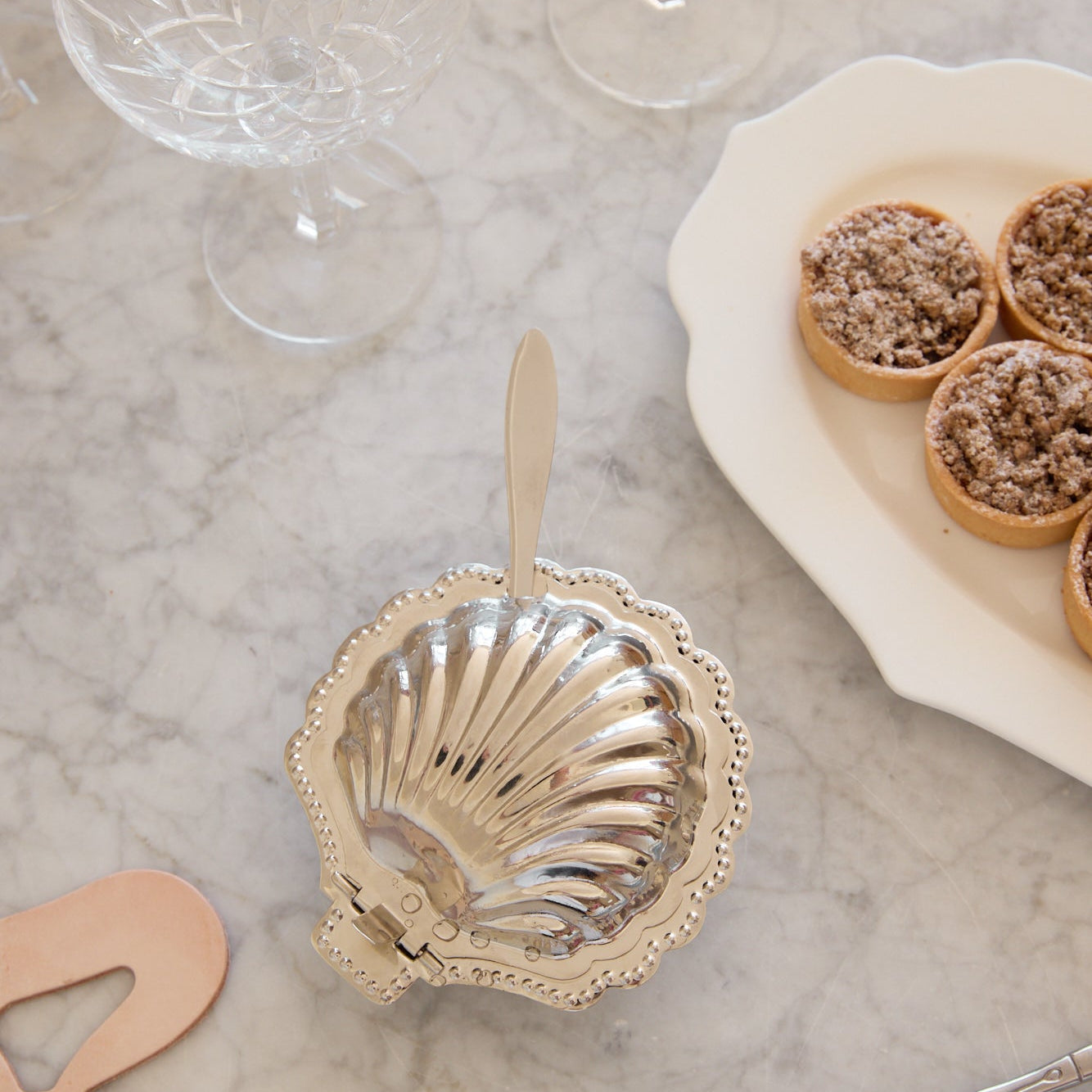 Decorative shell-shaped dish on a marble surface with glasses and pastries in the background