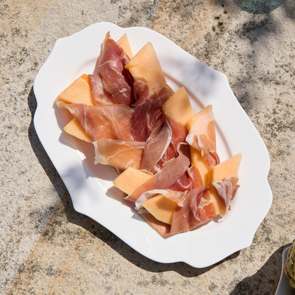 Platter of prosciutto-wrapped melon pieces on a stone surface