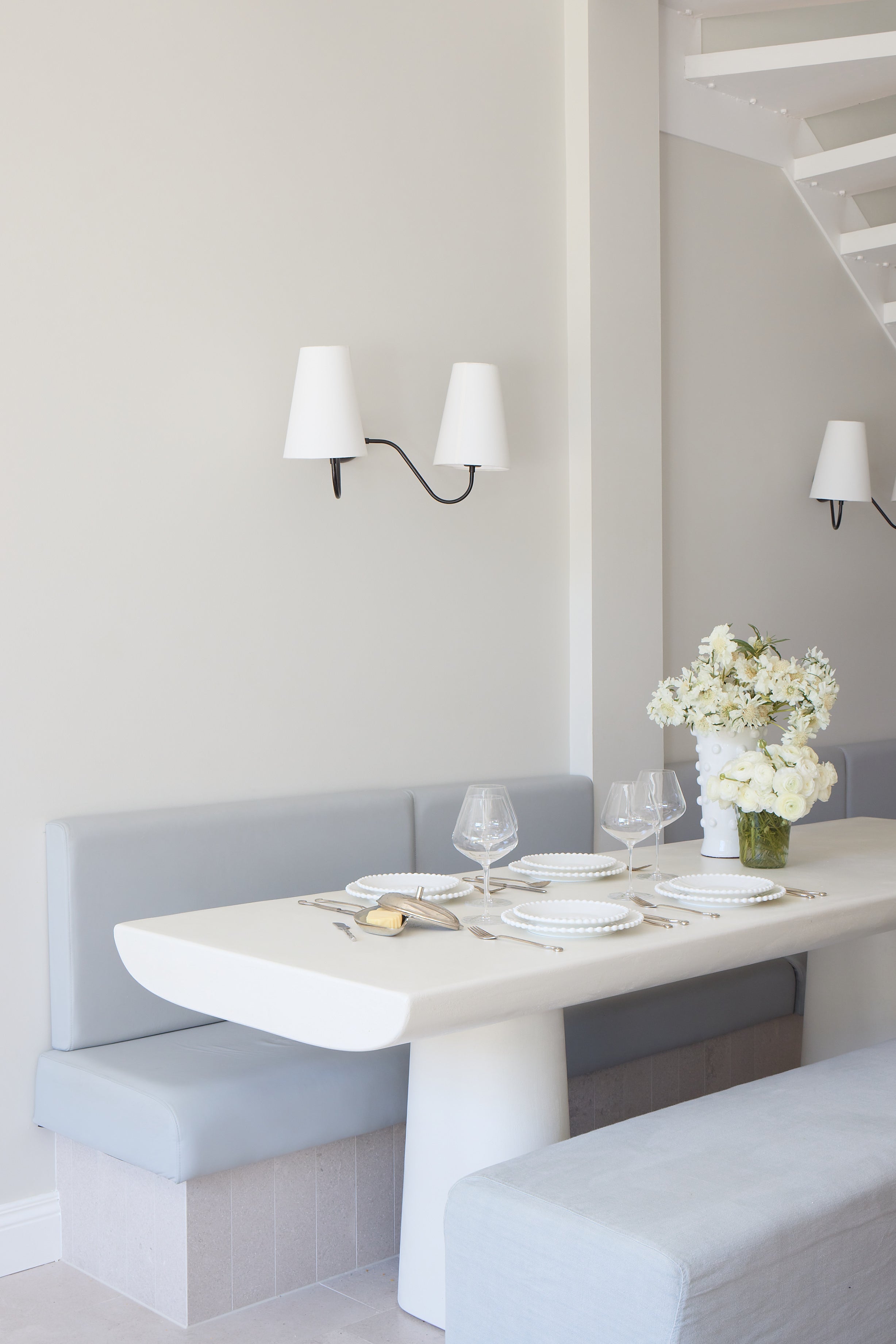 Modern dining area with a white table and gray benches against a light gray wall.