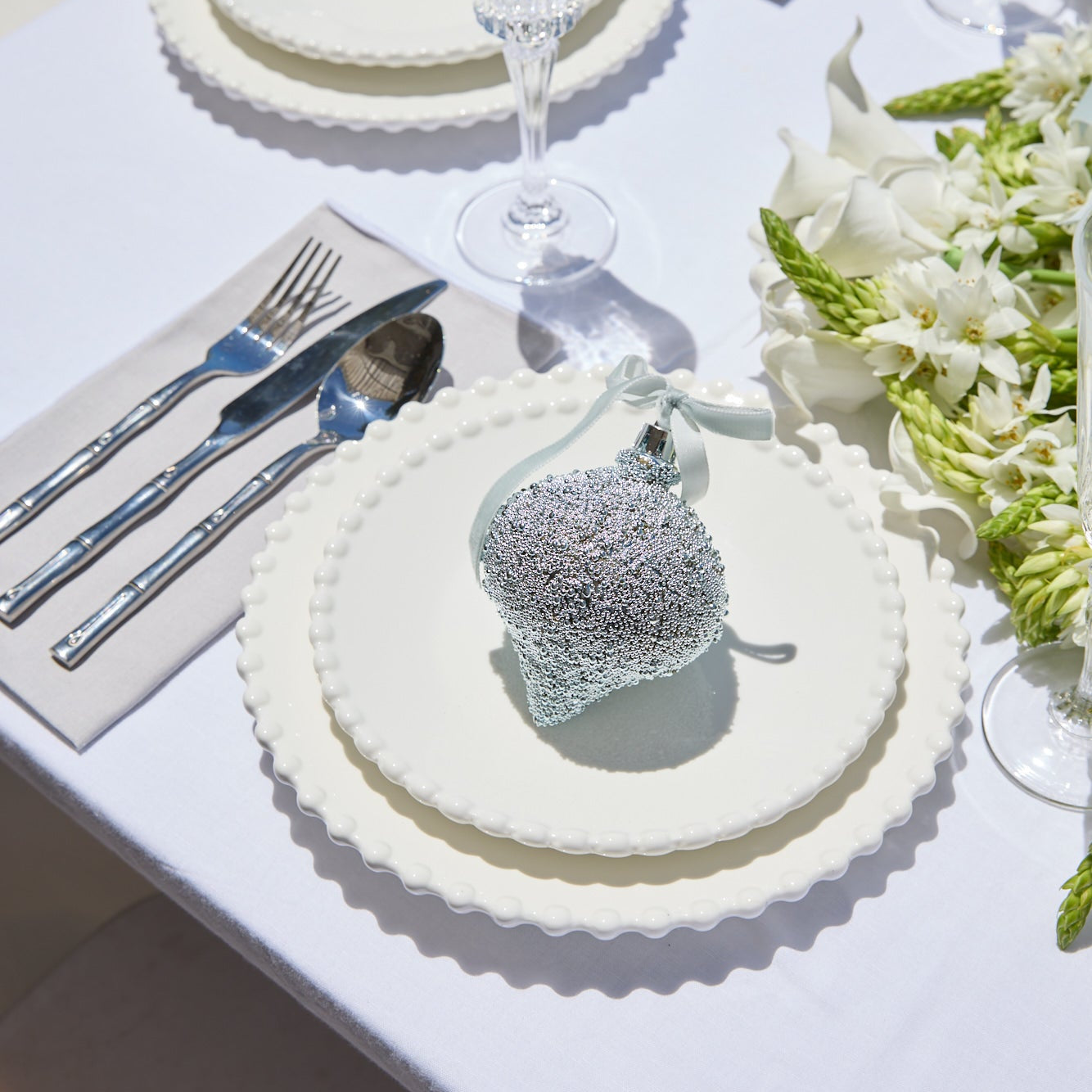 Elegant table setting with crystal glasses, silverware, and floral decorations on a white tablecloth.