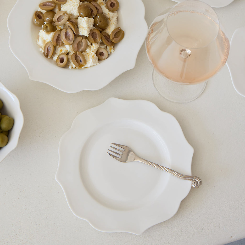 Dessert plates with various pastries and a glass of white wine on a light surface.