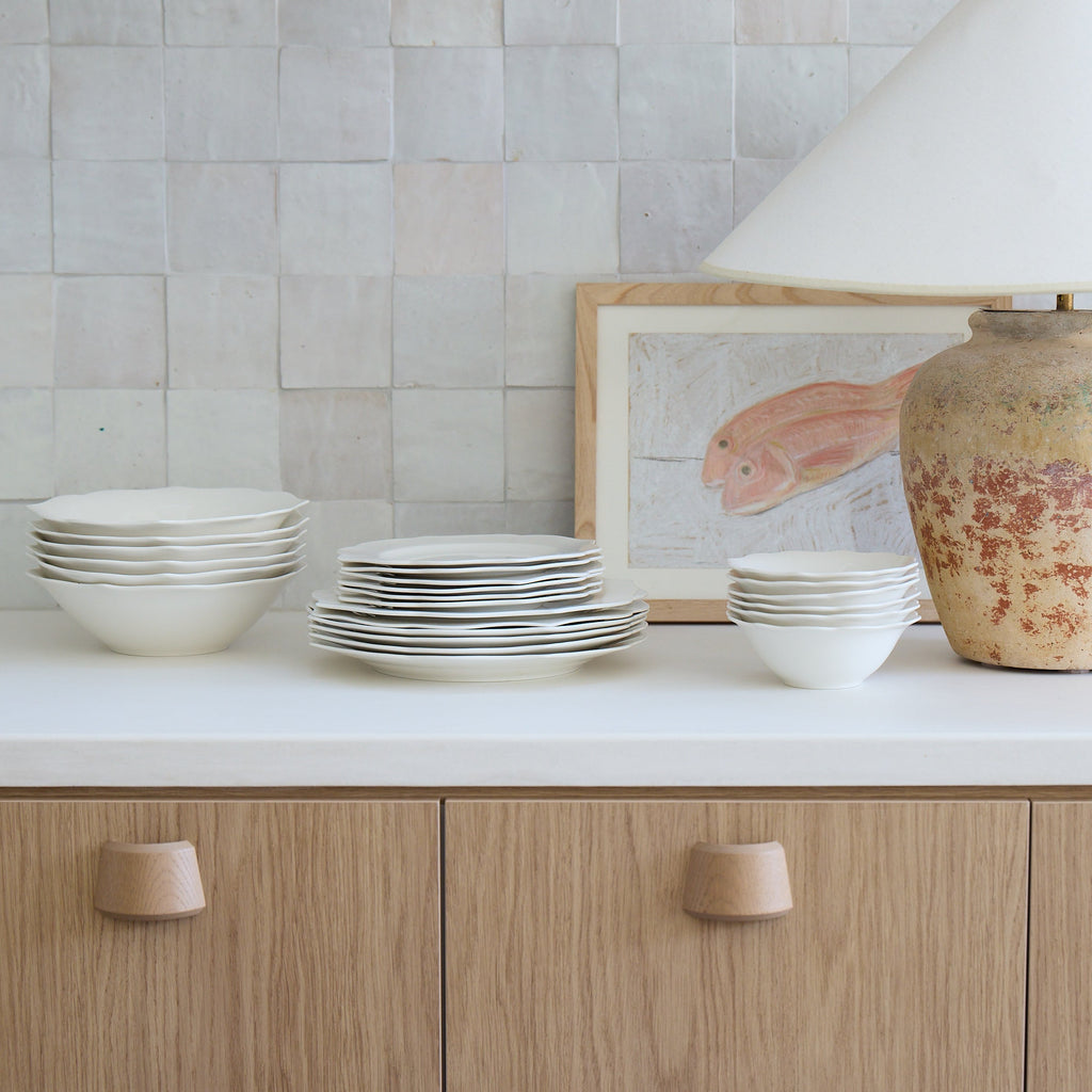 Ceramic tableware on a kitchen counter with a lamp and framed picture in the background.