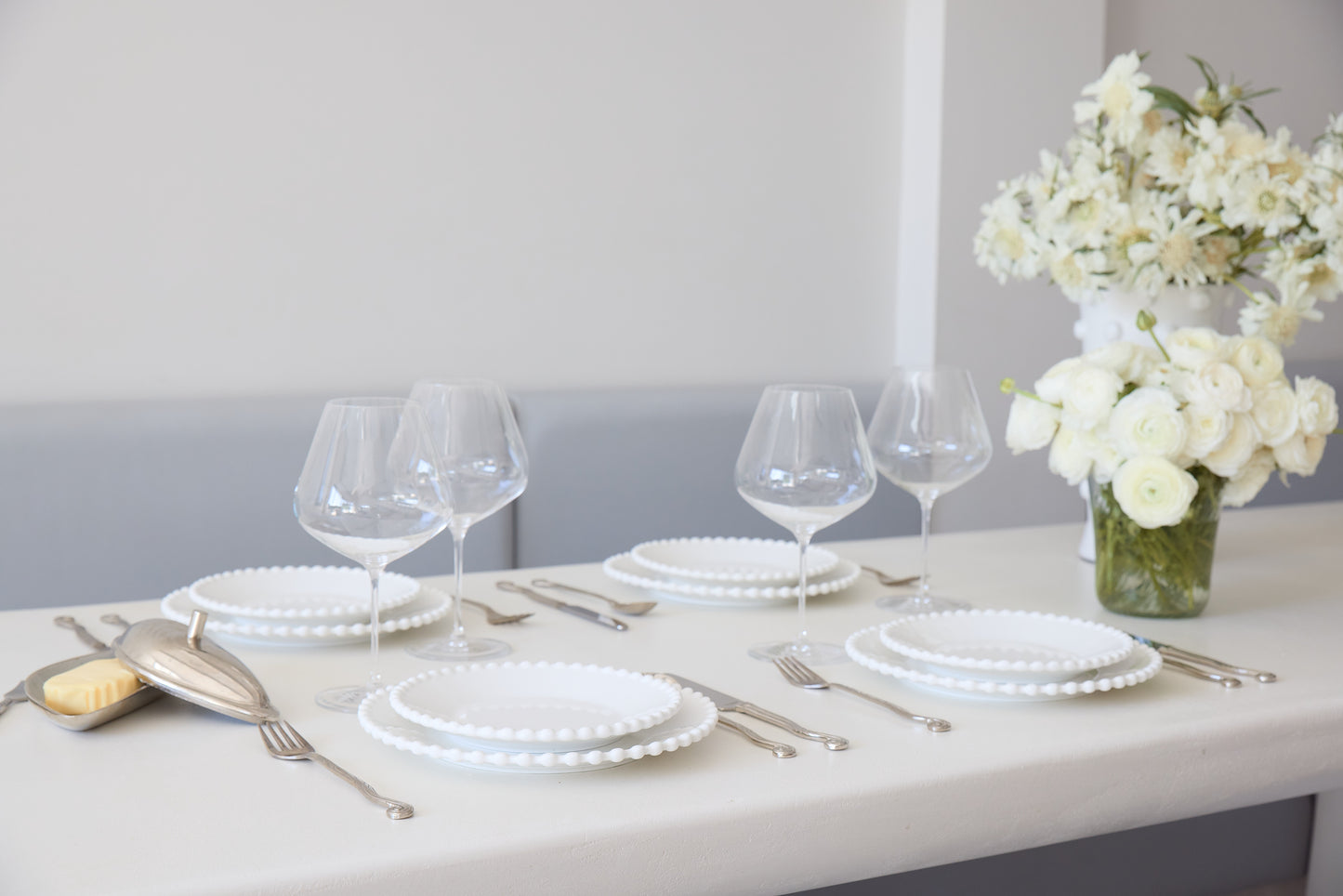 Dining table set with white plates, glasses, and silverware on a light surface.