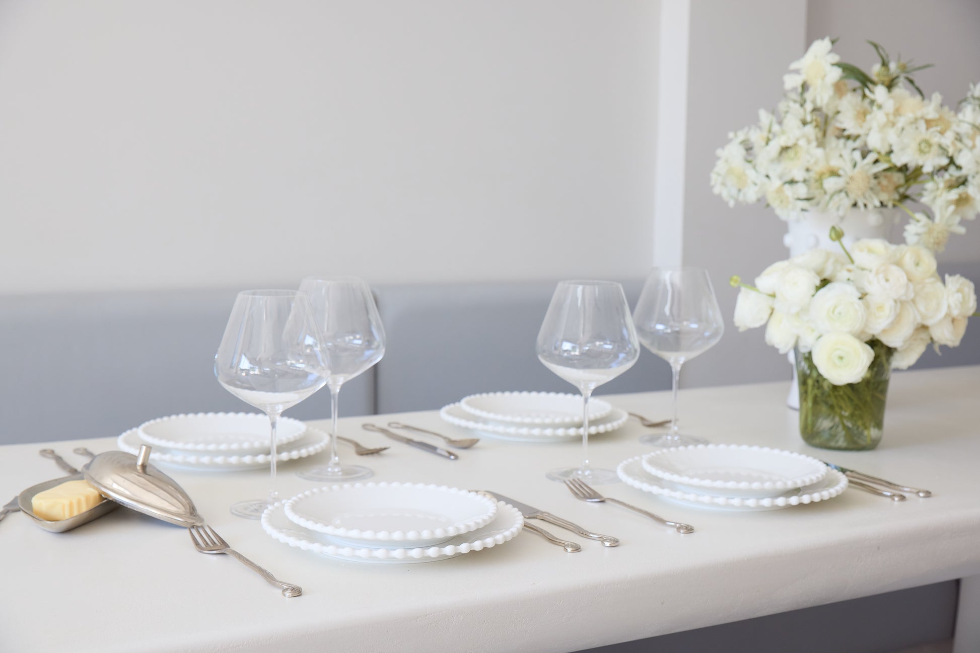 Dining table set with white plates, glasses, and silverware on a light surface.