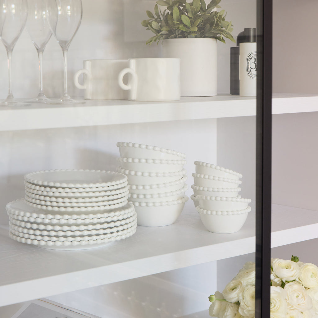 White ceramic plates and bowls on a shelf with a vase of flowers and a magazine.