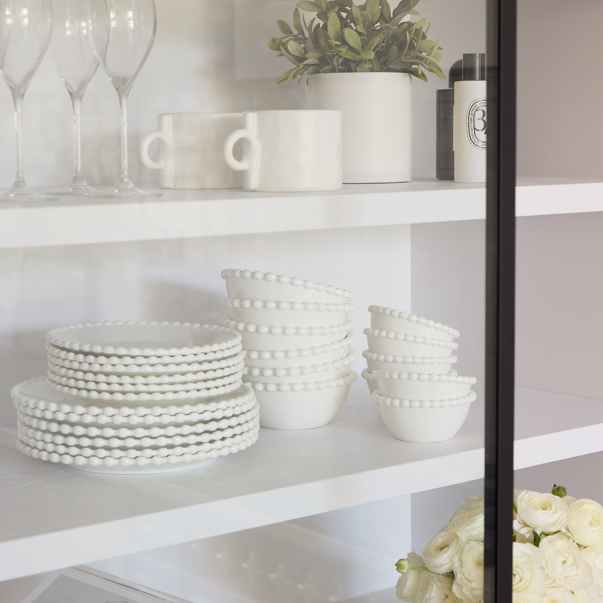 White ceramic plates and bowls on a shelf with a vase of flowers and a magazine.