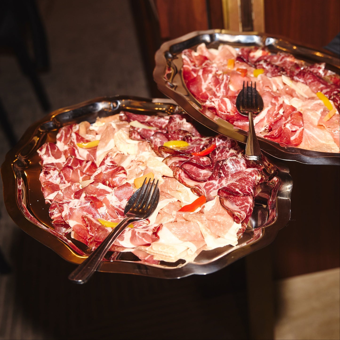 Two trays of sliced meat with forks on a dark background